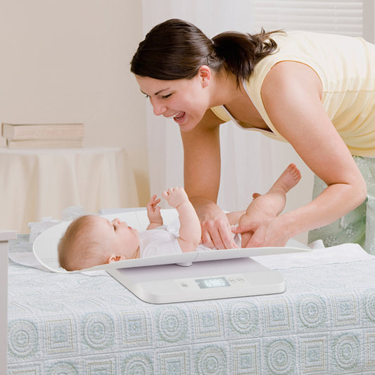 A mother smiling while placing her baby onto the white tray of the digital weighing device