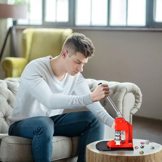 A man sitting on a sofa using the badge maker to create small pin buttons on a side table