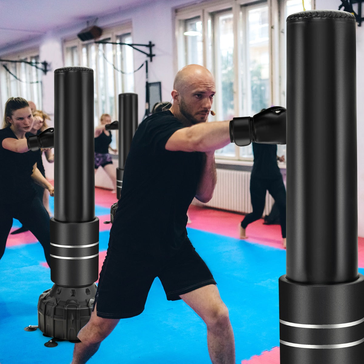 A boxing bag with boxing gloves and suction cup base in a gym setting with people training