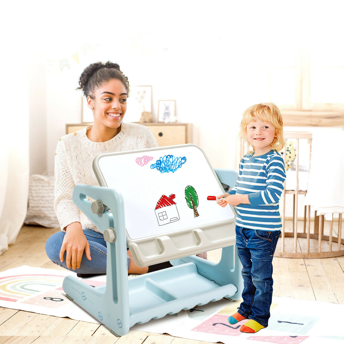 The art easel being used by a child drawing while an adult watches nearby