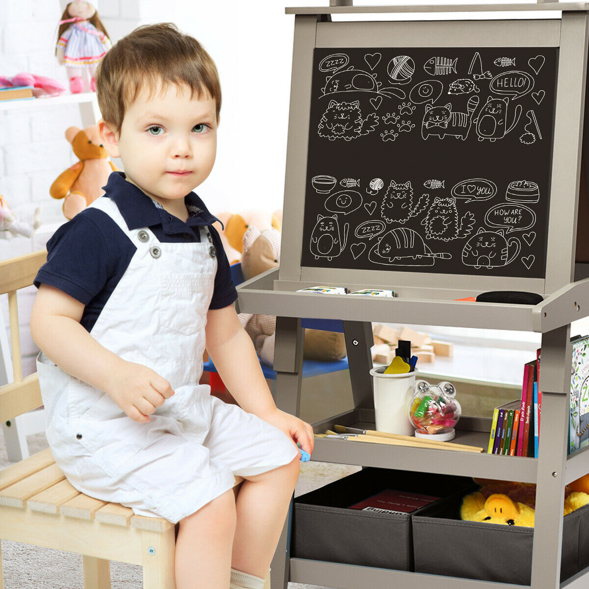 The art easel with a young boy sitting beside it while looking at the blackboard side