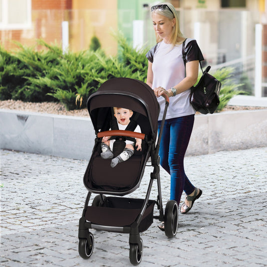 The baby stroller being pushed by a woman on a paved path with a baby sitting inside