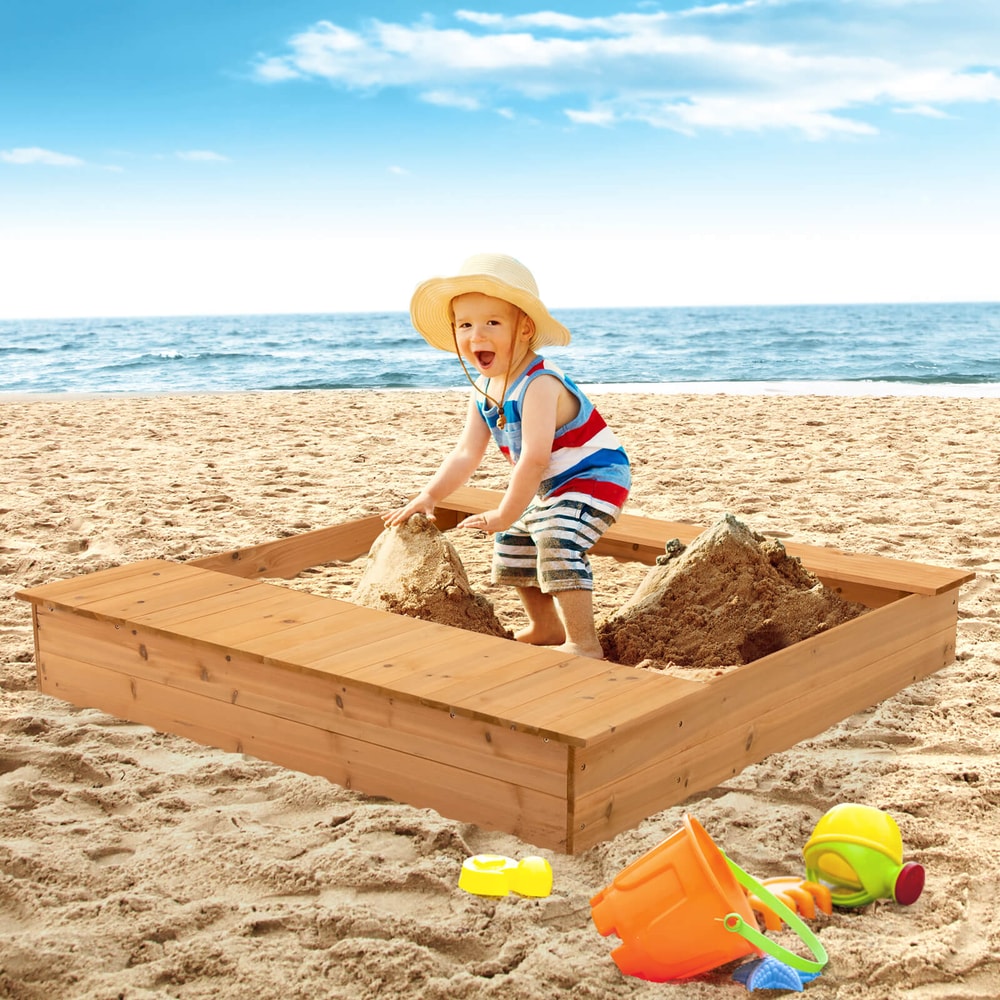 A young boy playing in the wooden sandbox on a sandy beach with the sea in the background