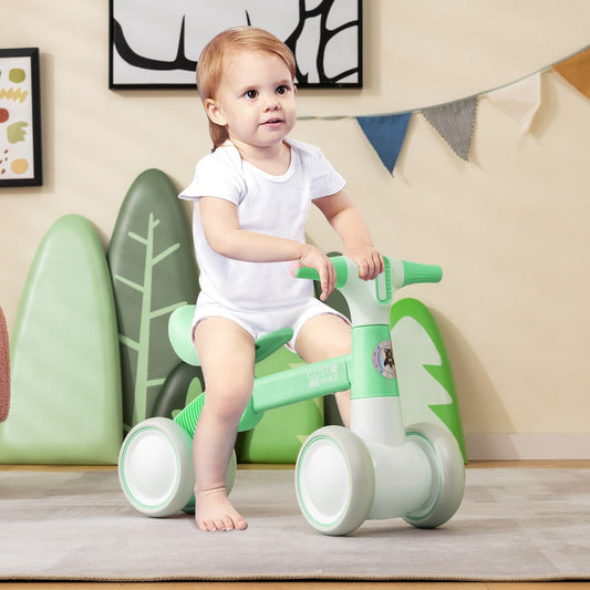 A baby sitting on the green balance bike indoors with a playful expression