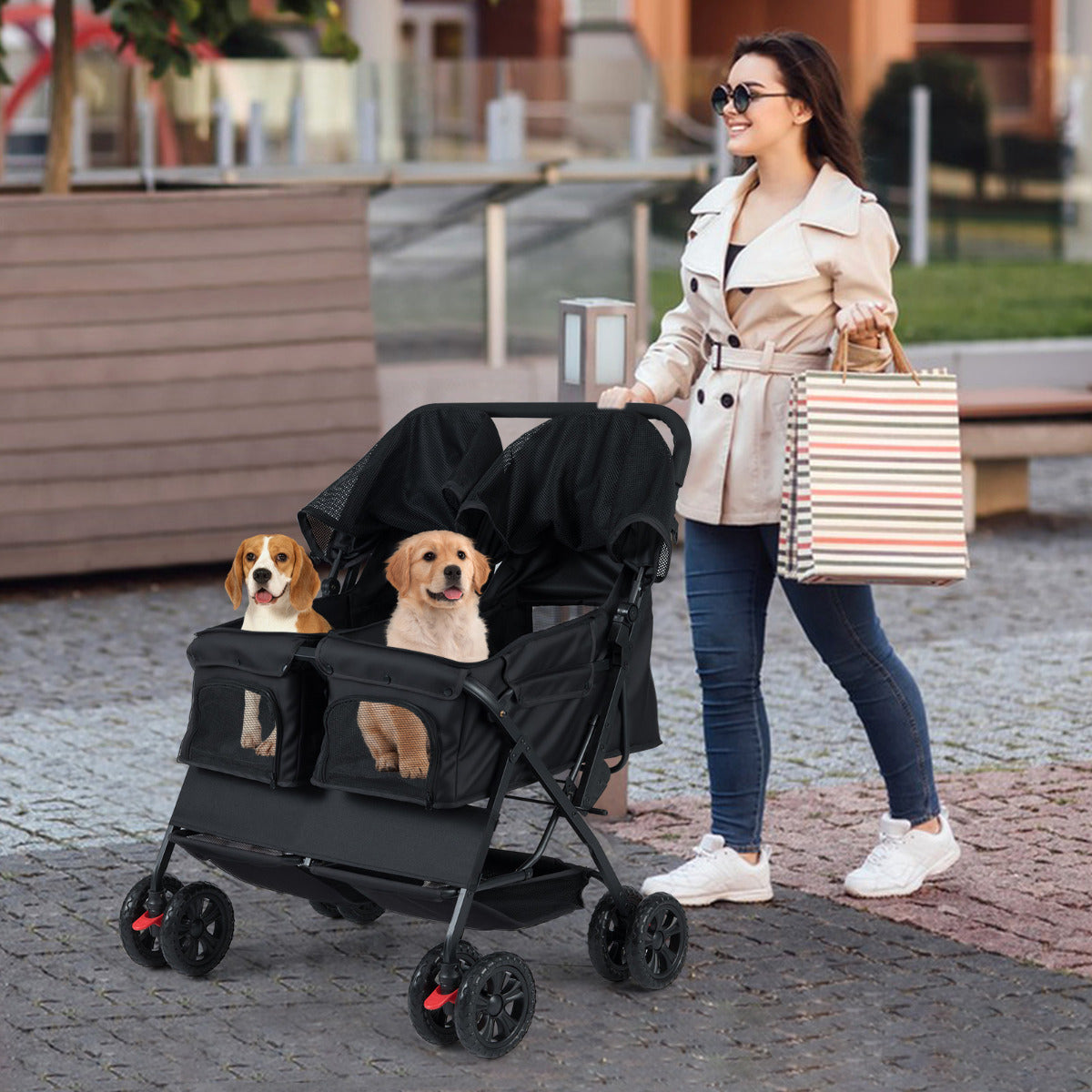 A woman walks with a black twin dog stroller carrying two dogs on a city pavement