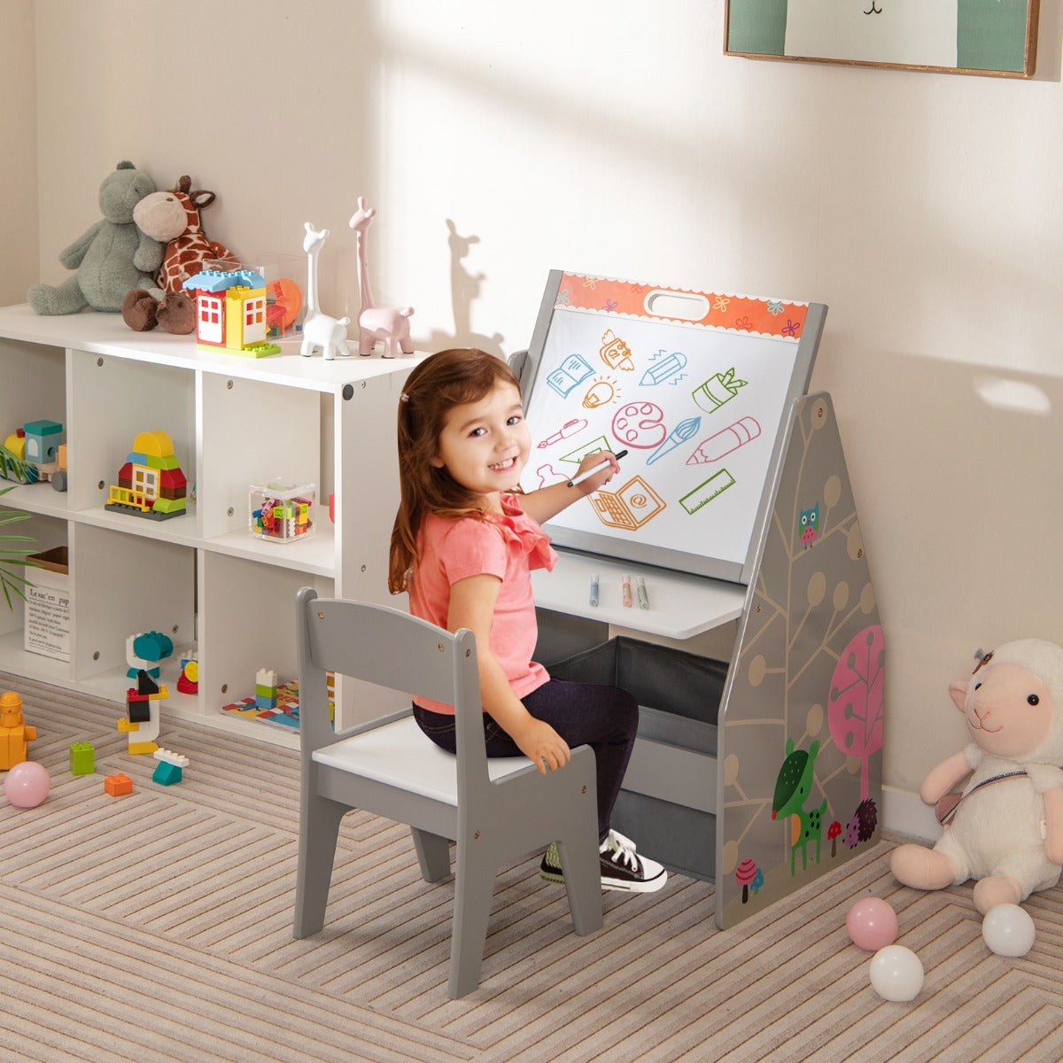 A young girl draws on the whiteboard of the art easel with a chair and storage bins