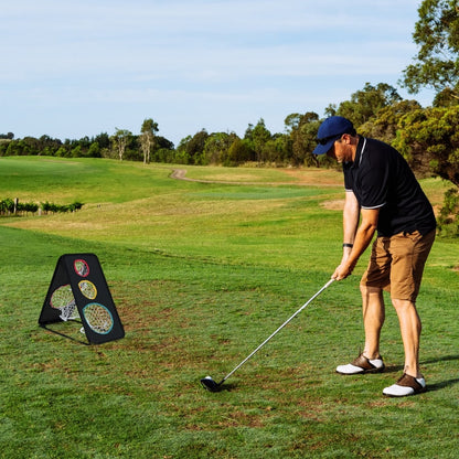 Man practising golf chipping into the net on a grassy field with trees