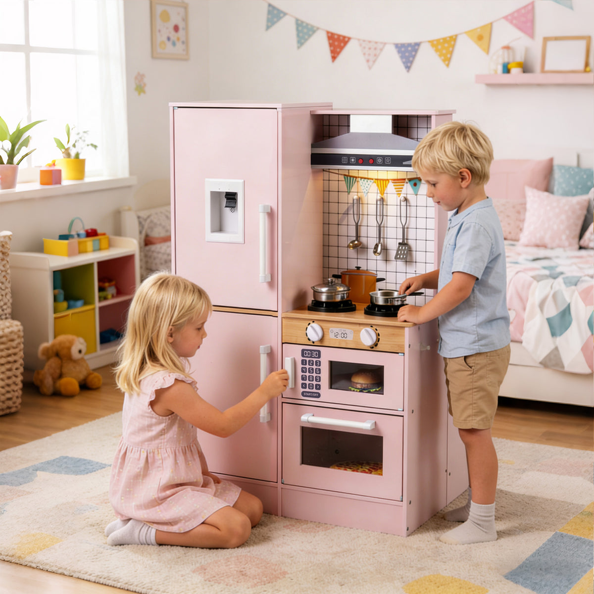 Two children play together at the pink dual-sided kitchen, one using the hob and the other the oven