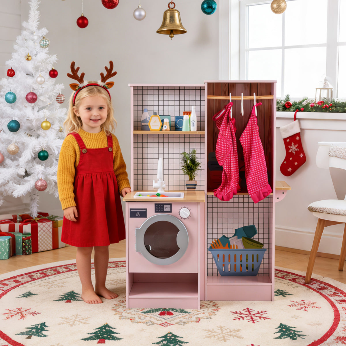 A young girl stands by the pink play kitchen, which is set up as a laundry area with a washing machine