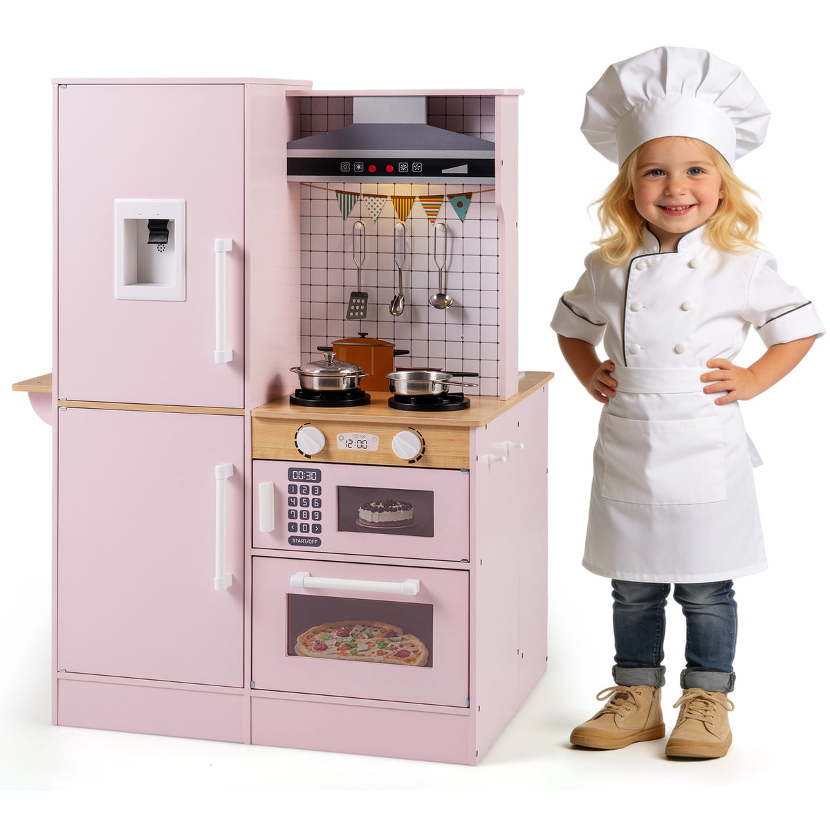 A little girl in a chef's outfit stands proudly next to the pink play kitchen set