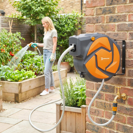 A woman waters plants in a garden with the wall mounted hose reel