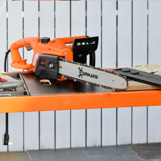 The electric chainsaw resting on a workbench in a garden setting with a white fence background