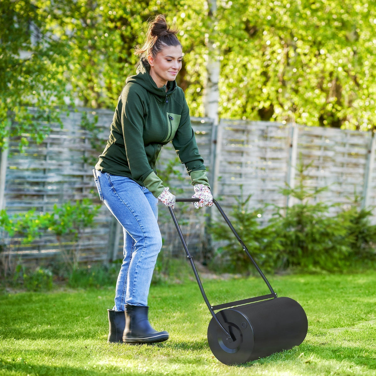 A woman uses the garden lawn roller to flatten grass in a garden