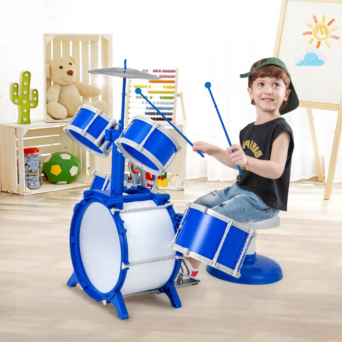 A young boy plays the blue drum kit in a room with toys