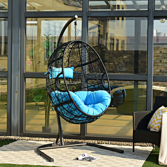 The turquoise egg swing chair with stand shown on a balcony with a black chair and plants