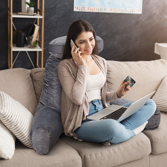 Woman using the grey reading pillow while on the phone and laptop on a sofa