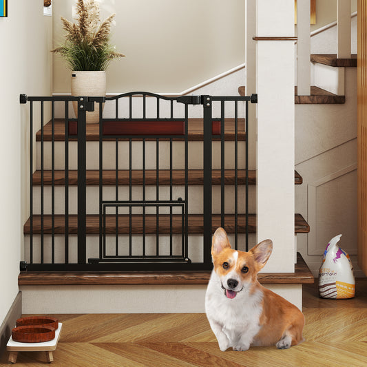 The black pet gate is installed at the bottom of a staircase with a corgi sitting in front