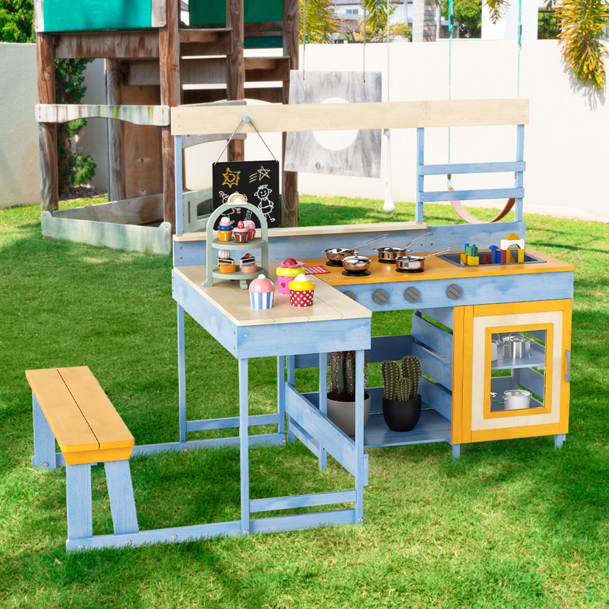 The blue and yellow mud kitchen with picnic table set up in a garden