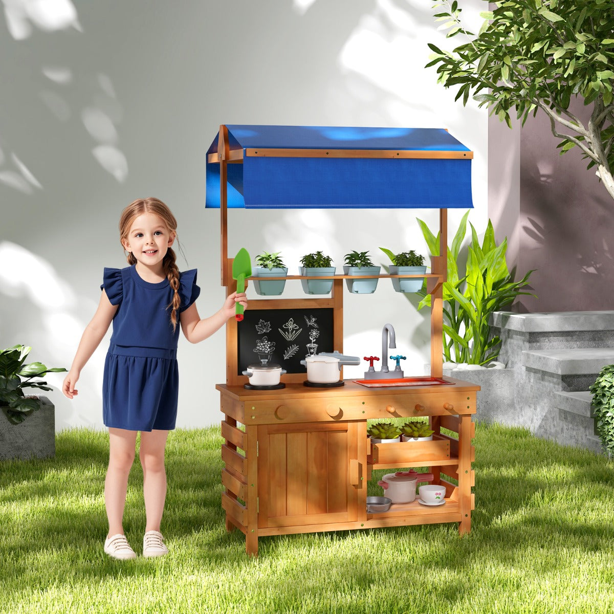 The play kitchen set standing on a grassy lawn with a young girl holding a green toy spade
