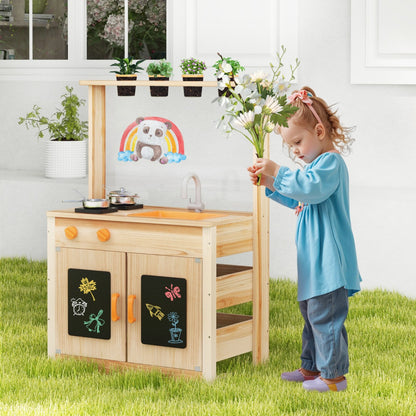 A young girl plays with flowers next to the wooden play kitchen set in a garden