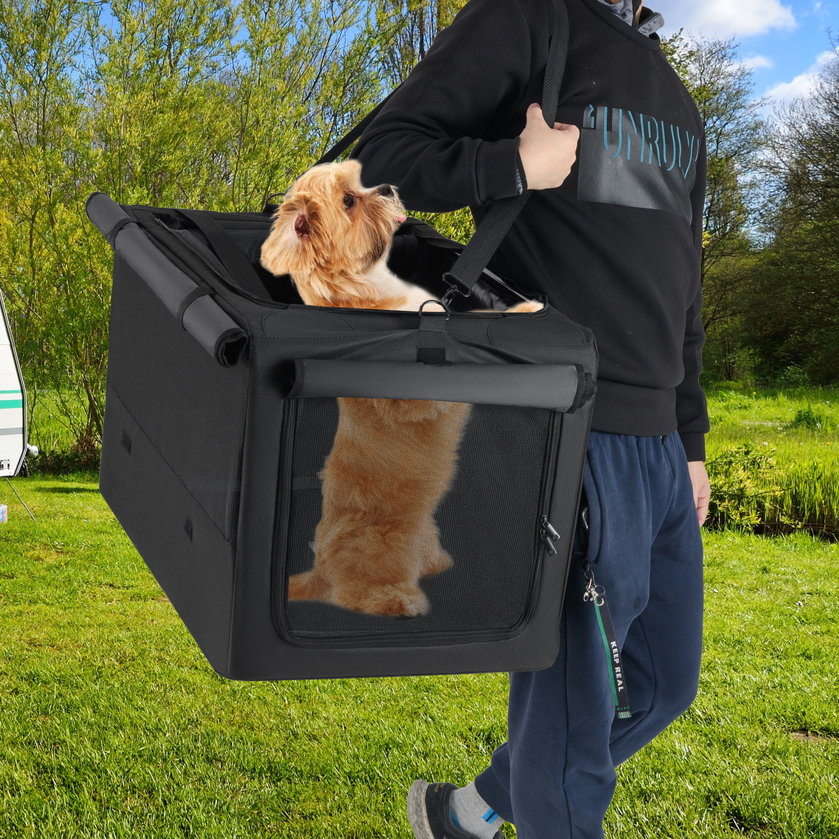 A person carrying the dog crate with a dog inside, outdoors in a grassy area
