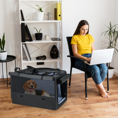 A woman working on a laptop next to the dog crate with a dog inside, in a home setting