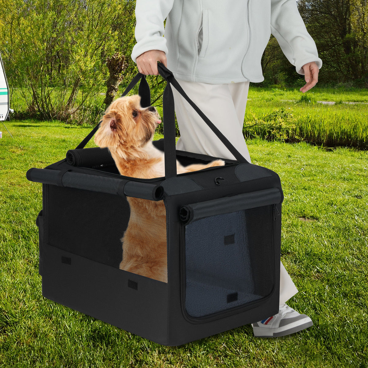 A person carries the dog crate with a dog inside through a grassy field