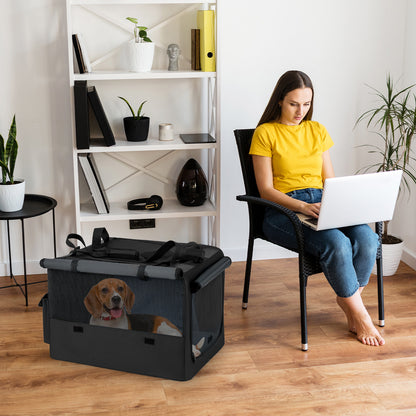 A woman sits on a chair using a laptop next to the dog crate with a dog inside