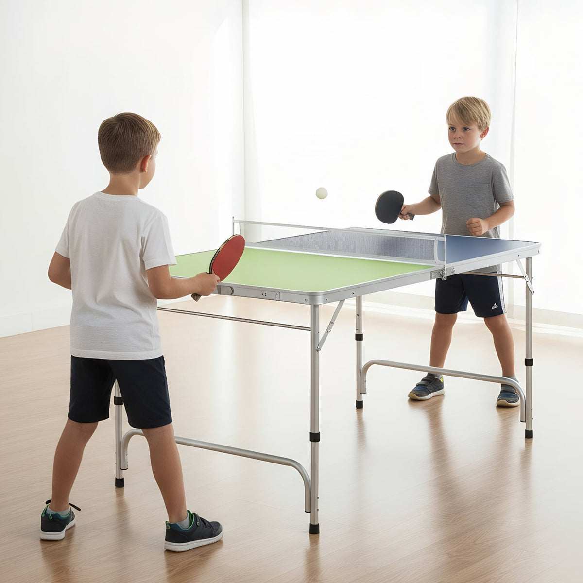 Two young boys playing table tennis indoors with the green and blue table