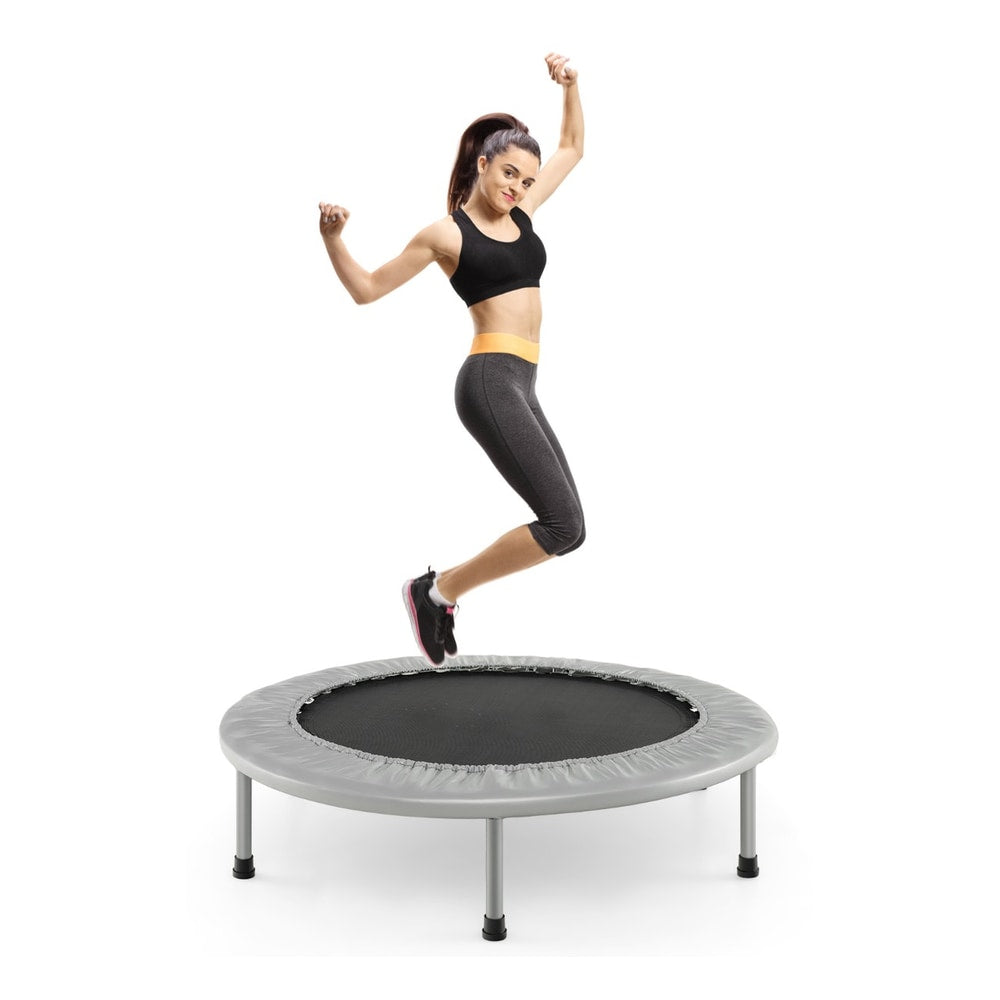 A woman mid-air jumping on the grey foldable mini trampoline against a white background