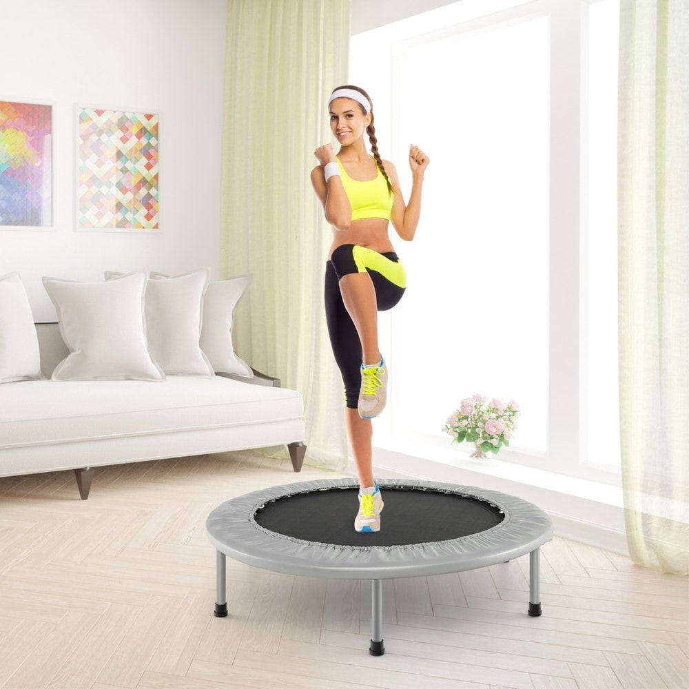 A woman doing a fitness routine on the grey foldable mini trampoline in a living room