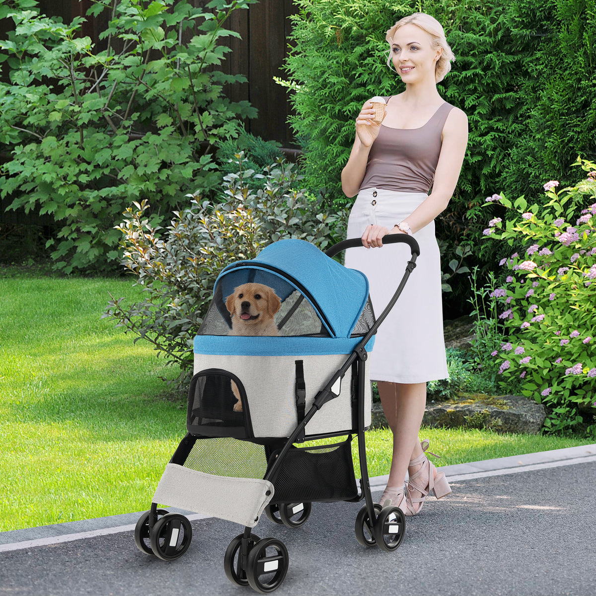 The dog stroller being pushed by a woman in a garden with a puppy inside