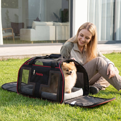 A red foldable pet carrier with wheels and a small dog inside, sitting on grass