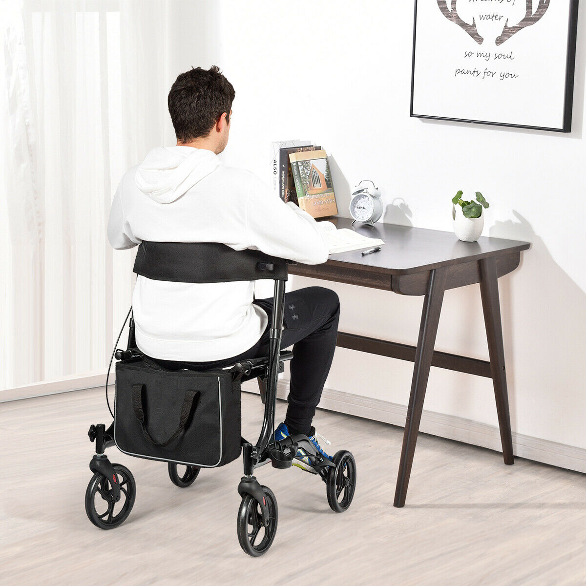The rollator walker being used as a seat by a man sitting at a wooden desk in a room
