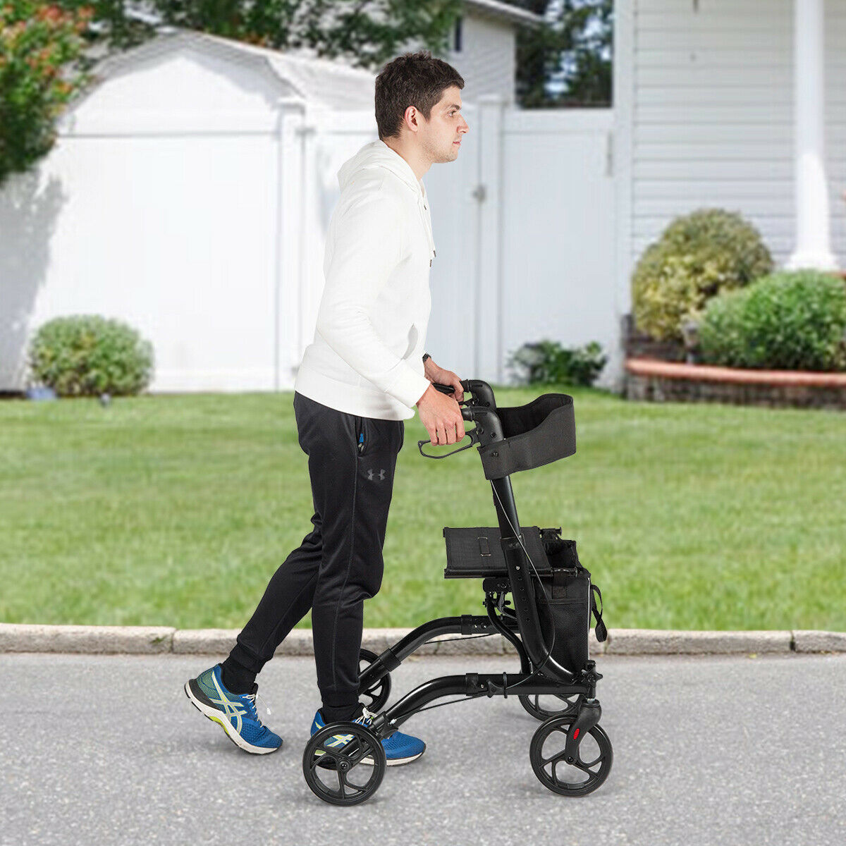 The mobility aid being pushed by a man walking along a paved path in a garden setting