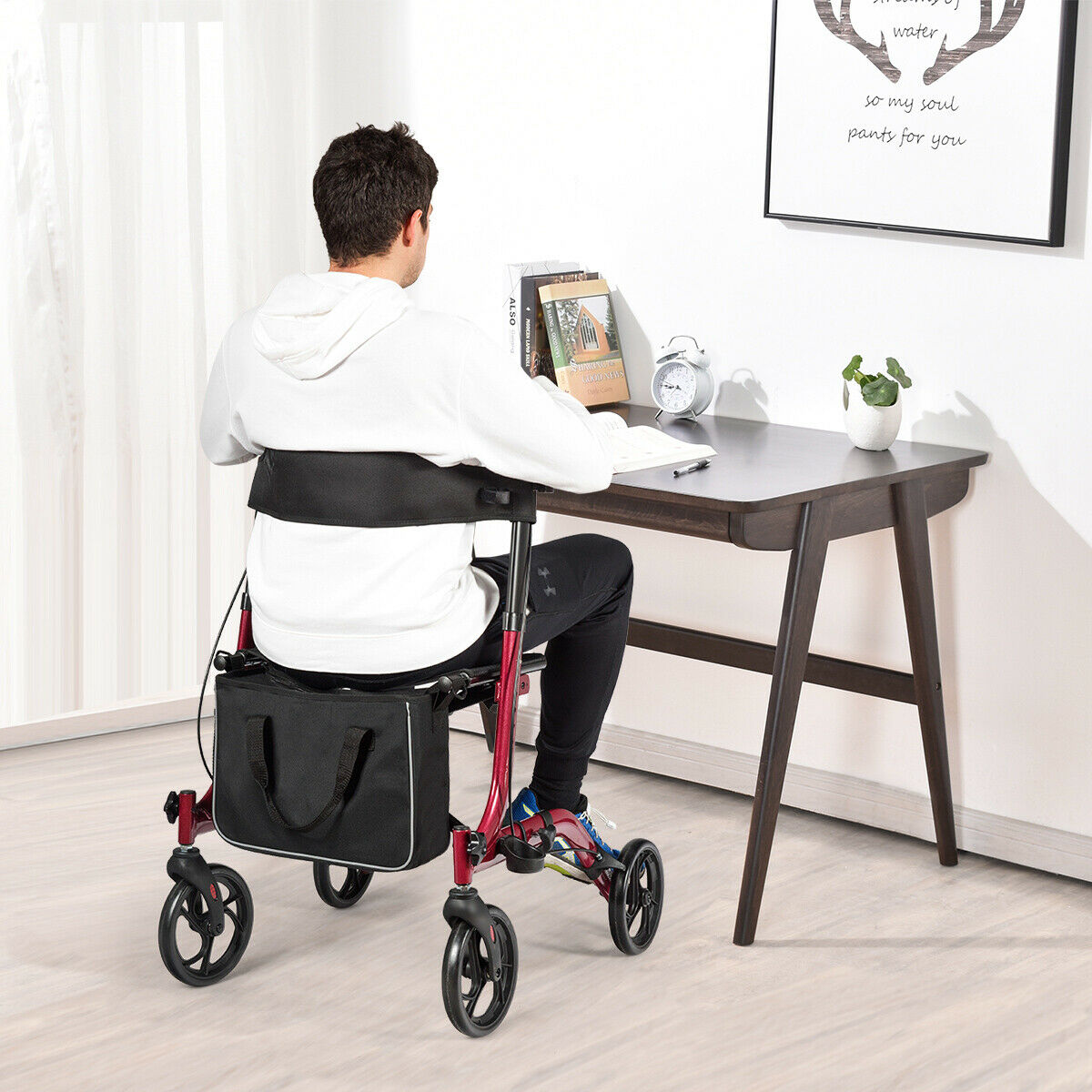 A man sits on the red walker with four wheels while working at a desk