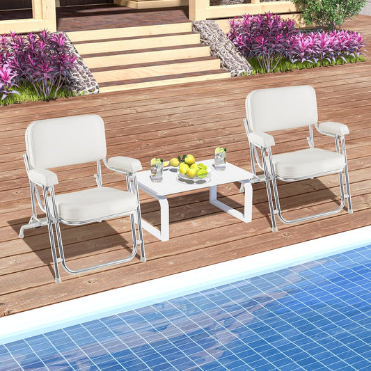 Two white upholstered deck chairs and a white table on a wooden deck by a pool