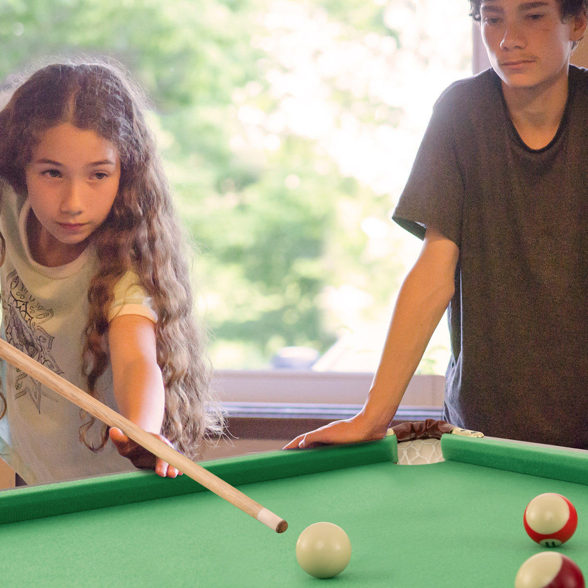 Two children playing billiards on a green folding table indoors