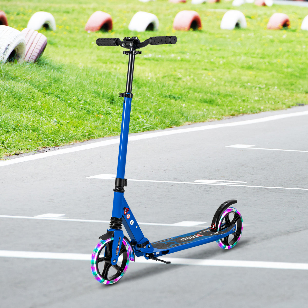 The blue kick scooter stands on a paved track with grass and barriers
