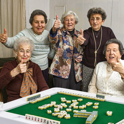 Four women sitting around the game table playing with tiles and giving a thumbs up
