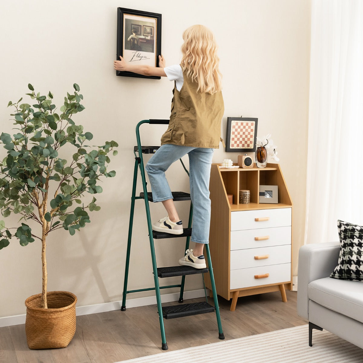 A person standing on the metal step ladder to hang a picture frame on the wall