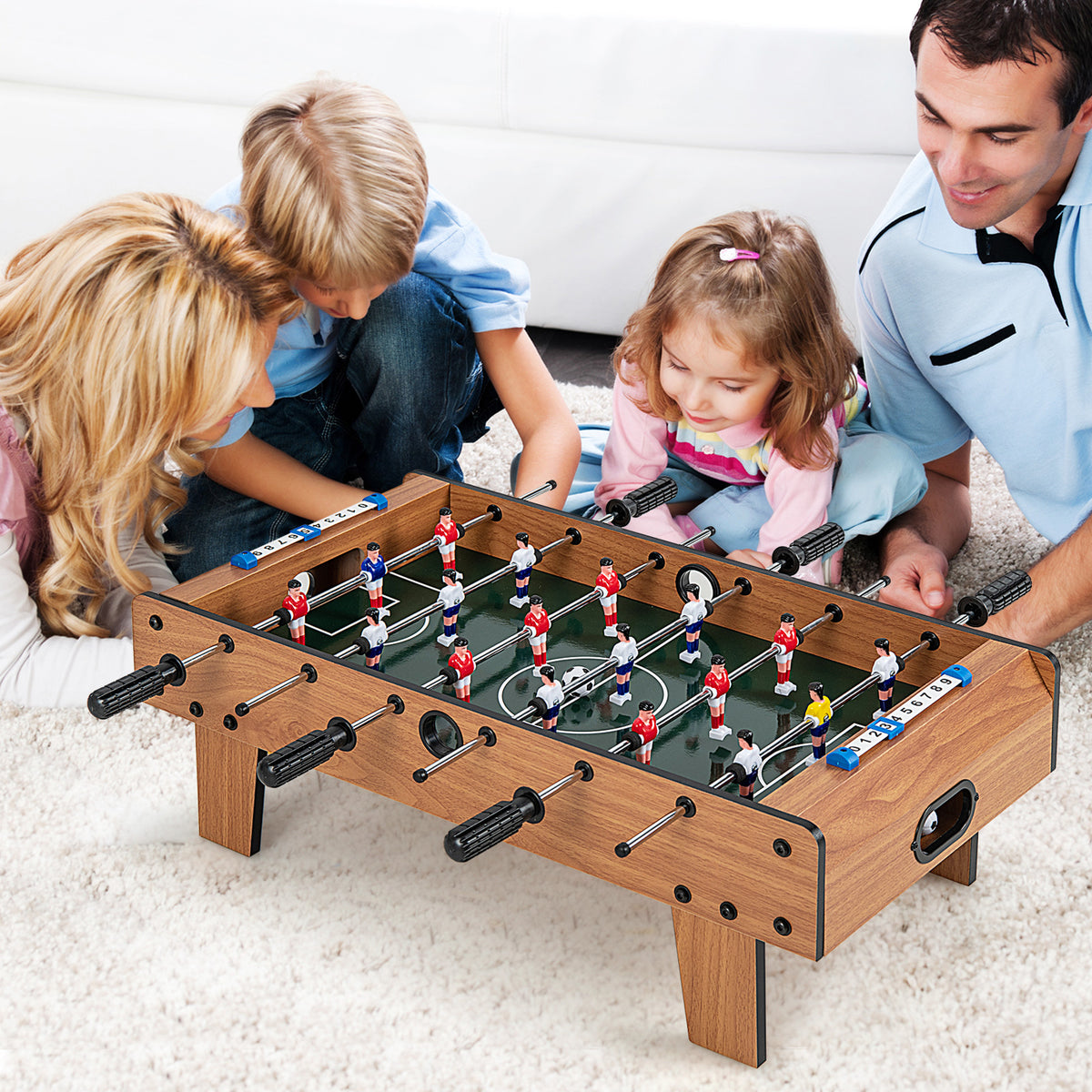 A family plays together on the football table on a living room floor