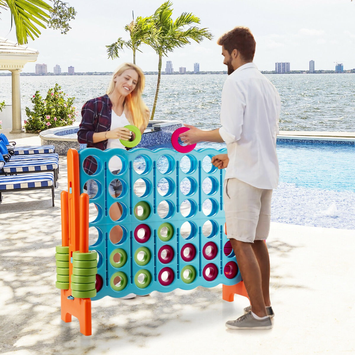 A couple playing the giant four in a row lawn game by a swimming pool
