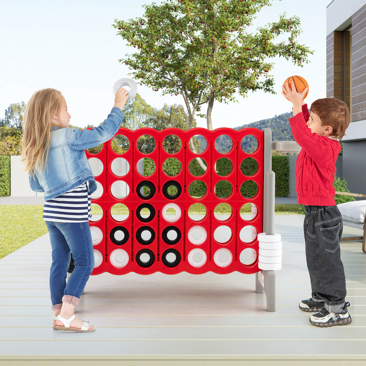 Two children playing the giant Connect 4 game on a patio outdoors