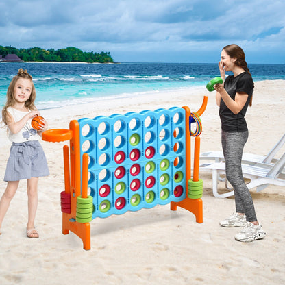 The lawn game is set up on a sandy beach with a woman standing next to it holding a green ring