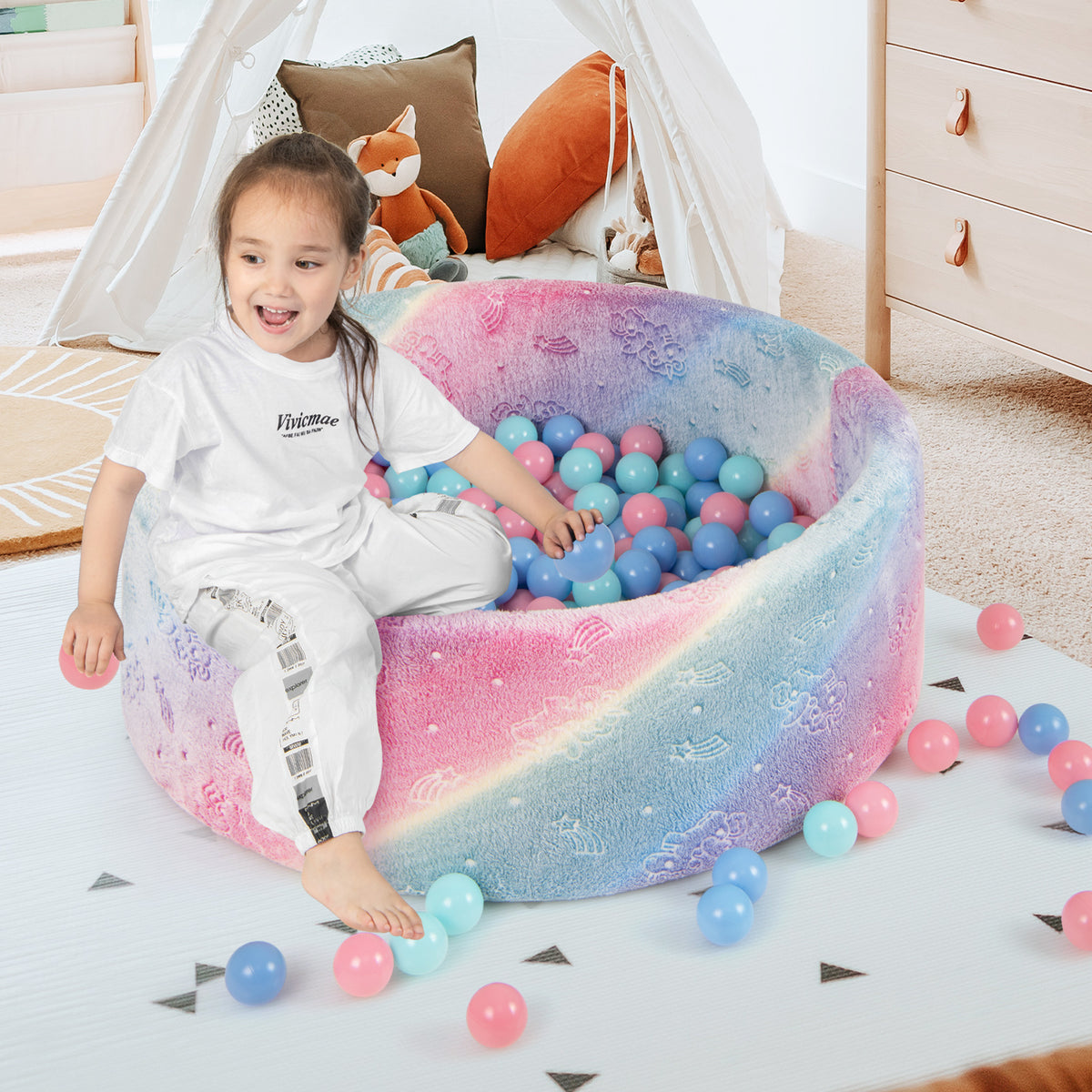 A young girl sits happily in the colourful round ball pool, which is surrounded by loose balls