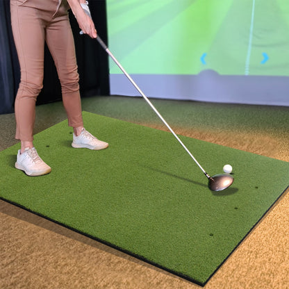 Woman practicing golf swings indoors on a golf hitting mat with a golf simulator screen
