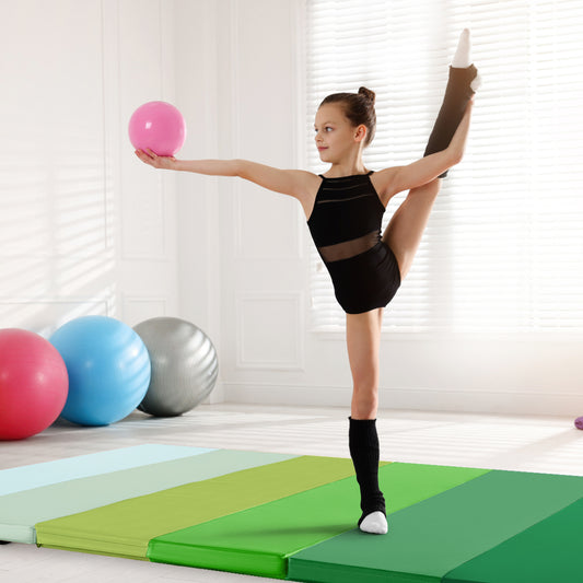 A girl in a leotard balances on a green gymnastics mat holding a pink ball