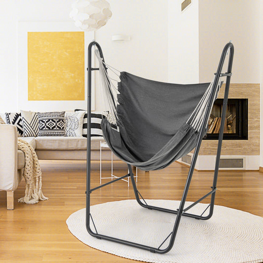 The hammock chair with stand is set up on a white rug in a modern living room with a sofa and fireplace