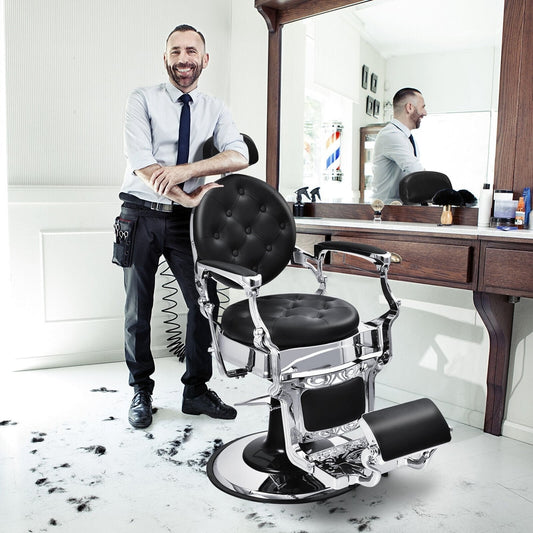A barber stands proudly next to the black salon chair in a room with scattered hair clippings